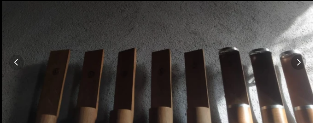 Row of rug-making tools lined up on a concrete wall